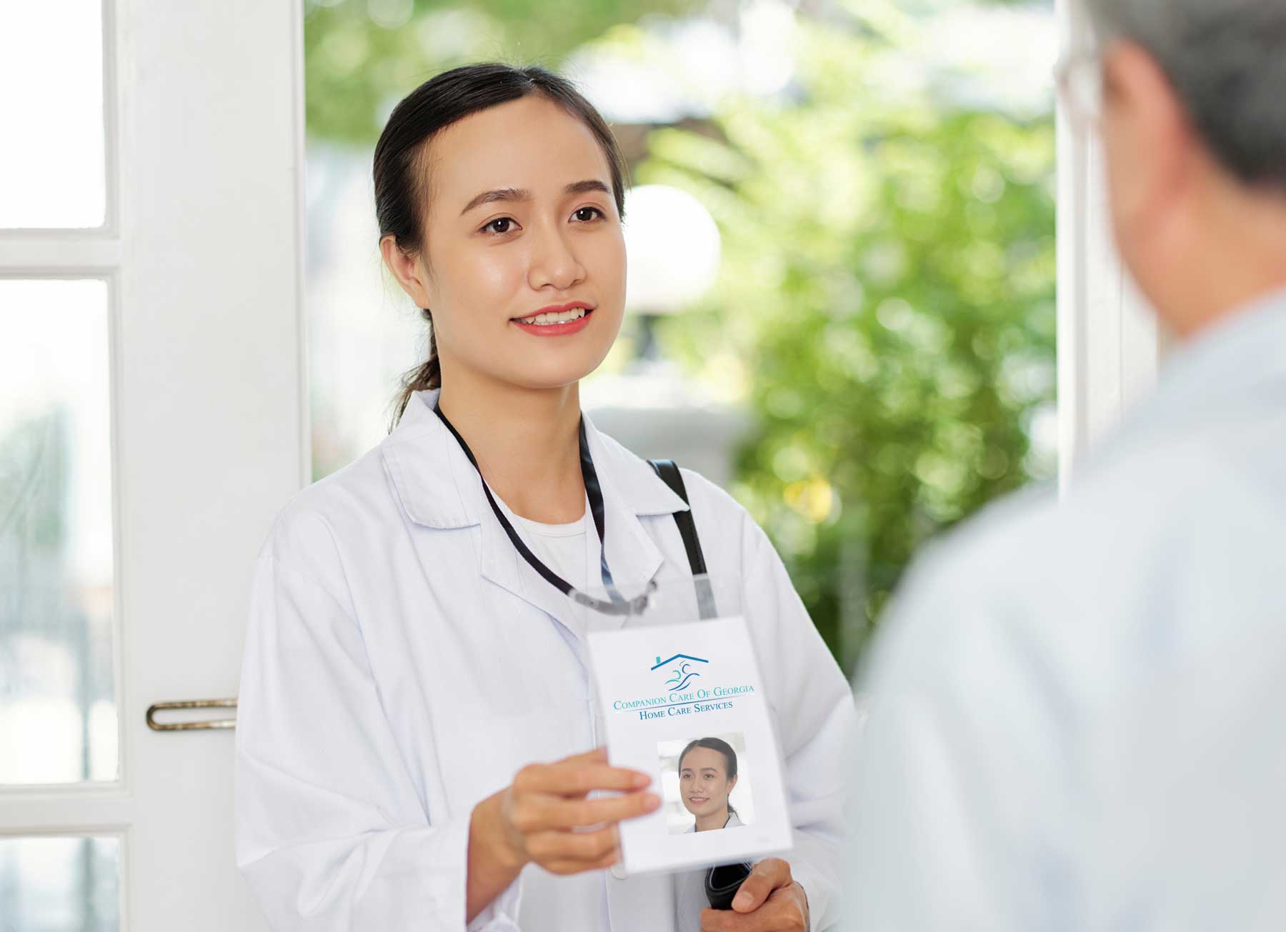 On a hot day, the sun blurs the neighborhood background. A nurse in Metter GA stands at the threshold of a front door holding out a photo ID to a man. She is a home health nurse, introducing herself as she arrives at a home for skilled medical services.