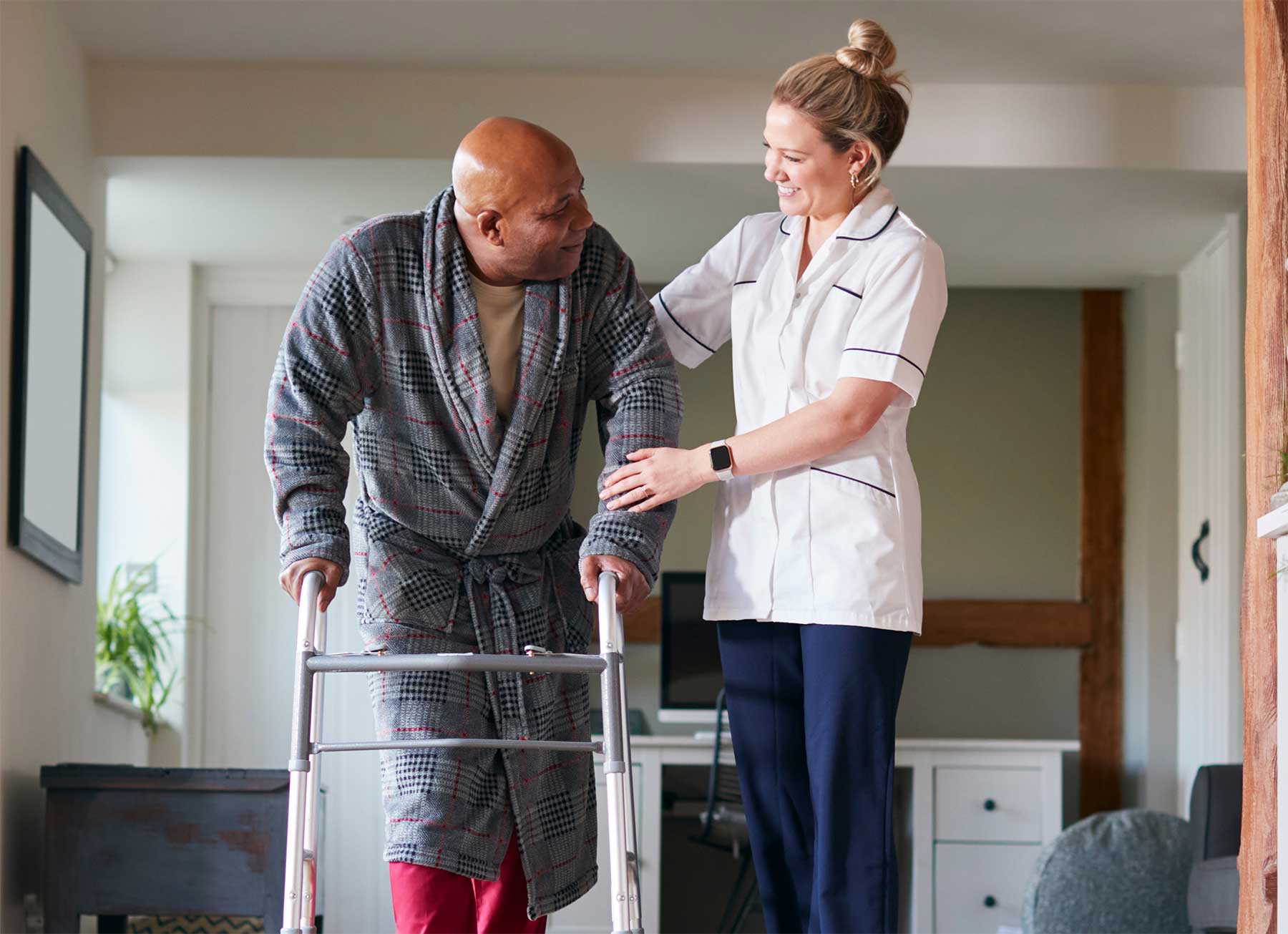 A home care aide in Metter, GA helps steady a senior who is managing a walker over the hardwood floors of his Central GA home. He smiles at her gratefully, as she smiles back with campassion and happiness.
