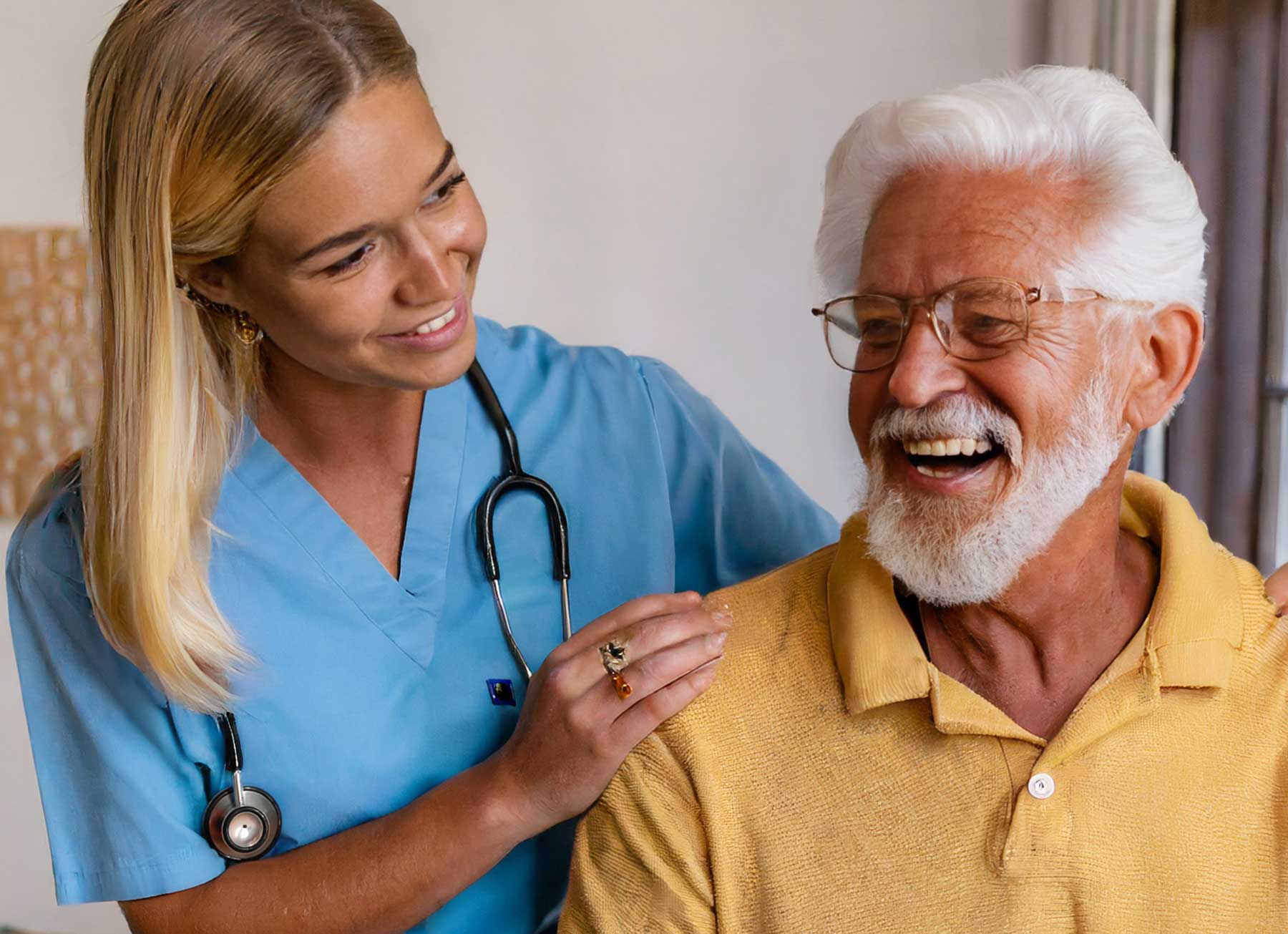 A white-haired senior in Brunswick, GA is sitting and luaghing, seemingly care free. Behind him, a nurse, dawned in blue scrubs and with a stethoscope draped around her neck, embraces the man loosely by placing a hand on each of his shoulders and smiling back at him. They demonstrate and obvious rapport that comes from caring and trust.
